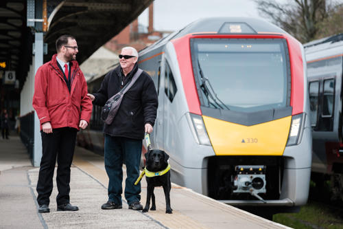 Visually impaired person assisted by greater anglia employee on a train platform